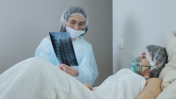 Paciente com covid-19 com máscara de oxigênio na cama do hospital, conceito de coronavírus. Médico olha e discute os resultados da tomografia computadorizada do paciente — Vídeo de Stock