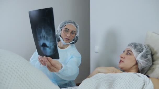 Dokter die de resultaten bekijkt en bespreekt van computertomografie van een patiënt die op een bed ligt in een spoedeisende hulp — Stockvideo