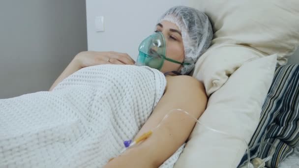 Een zieke jonge vrouw ligt op de afdeling in een zuurstofmasker en trekt abrupt een druppel, intraveneuze zoutoplossing, een oplaaddosis uit haar hand — Stockvideo