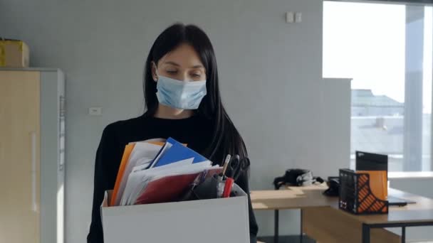 Jeune femme portant un masque tenant une boîte d'effets personnels quittant ses fonctions après avoir perdu son emploi crise économique et chômage lors de l'épidémie de covidé-19. — Video