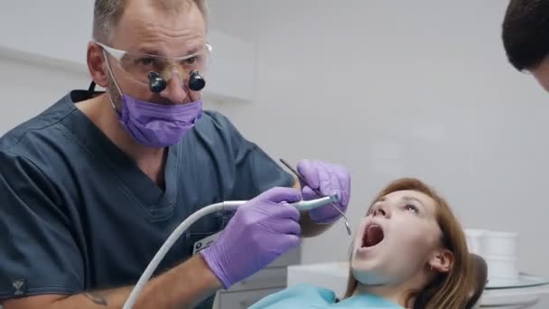 Dentysta w sterylnych rękawiczkach leczący pacjenta za pomocą wiertarki. Profesjonalny dentysta wiercący zęby klientowi. opieka, leczenie — Wideo stockowe