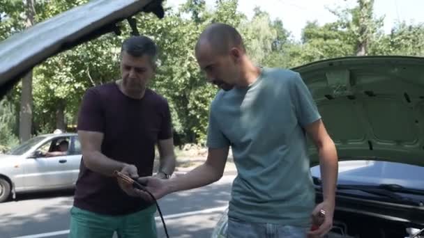Φόρτιση μπαταρίας αυτοκινήτου. Άνδρες στέκονται κοντά στο αυτοκίνητο άνθρωπος βοηθώντας φίλο φόρτισης αυτοκινήτου μπαταρία — Αρχείο Βίντεο