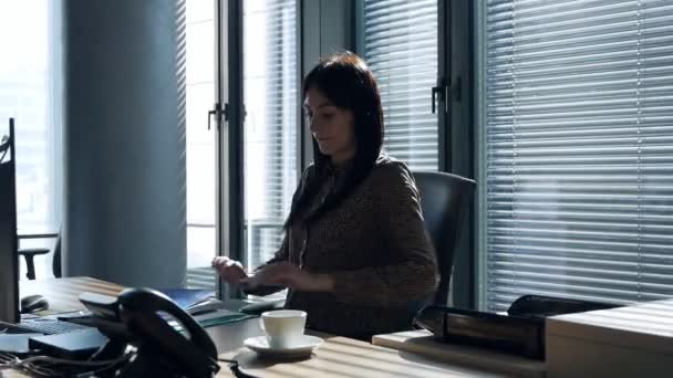 Young female worker in industrial espionage concept. The secretary puts coffee on the table in the office and looks for the necessary documents, and then photographs them — Stock Video
