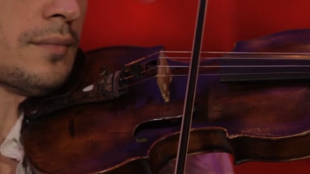 Un joven toca el violín sobre un fondo rojo — Vídeos de Stock