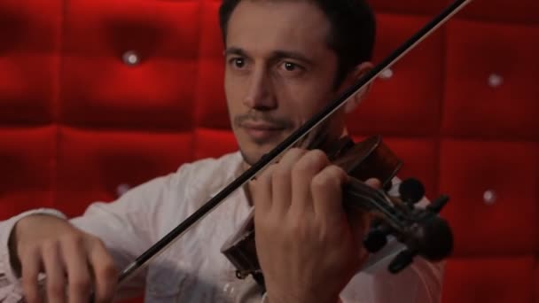 一名年轻男子在红色背景上拉小提琴 — 图库视频影像