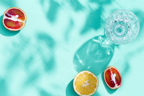 Composition with slices grapefruit, red orange, lemon and drink glass on turquoise color. Summer time flat lay