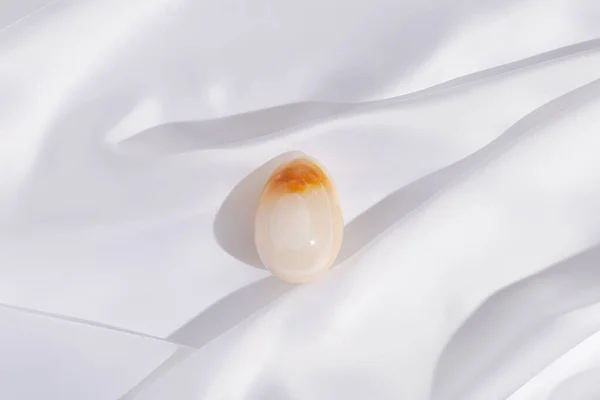 Ovos de Páscoa feitos de ônix de pedra preciosa natural no fundo de textura de pano branco. Arranjo de férias na primavera na moda. — Fotografia de Stock