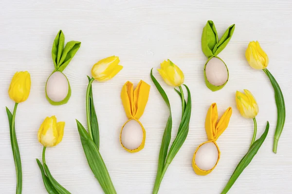Húsvéti tojás mókás fülekkel nyúl és tavasz sárga friss virágok tulipán fa asztalon — Stock Fotó