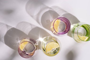 Beyaz arka planda turunçgil dilimli ferahlatıcı su dolu renkli bardaklar. Yaz kreatif düzlük