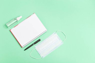 Öğrenciler için kişisel koruyucu malzemelerle yatıyordu. Yüz maskesi, el dezenfektanı, defter, yeşil renkli kağıt üzerine kalem. Üst görünüm, kapat, alanı kopyala.