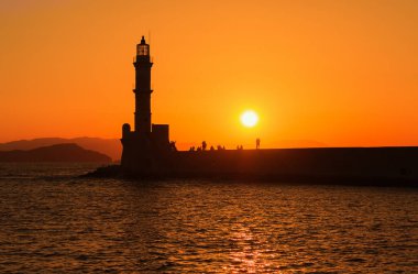 Girit, Yunanistan 'daki Chania' daki deniz fenerinin manzarası. Batan güneşe karşı siluetler.