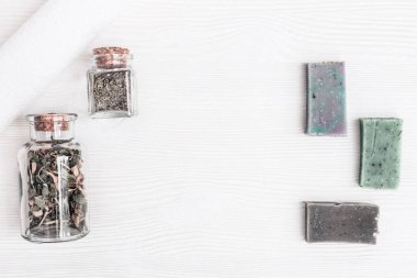 Doğal aromatik katkı maddeleri olan el yapımı sabunlar, beyaz pamuk havlu ve ahşap masada fotokopi alanı olan organik otlarla dolu küçük şişeler. Aromaterapi, güzellik merkezi. Üst görünüm. 