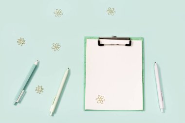 Ofis malzemeleri, ataçlı kağıt tablet, mavi ve beyaz renkli kalemler, cetvel ve metal kağıt raptiyelerle yatıyordu..