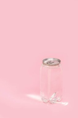 Pembe arka planda güneş ışığı olan şeffaf bir teneke su. Monokrom görüntüsü. Yaratıcı fikir, plastik şişede temiz su paketi..