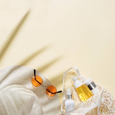 Güneş şapkası, renkli güneş gözlüğü ve kumlu arka planda beyaz şişede kozmetik ürünler olan yaz minimumu. Yaz konsepti pastel renkli estetik fotoğraf.