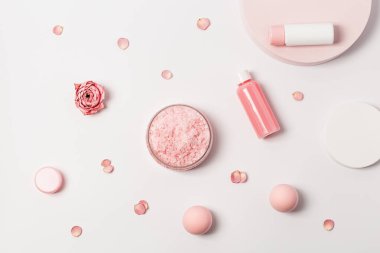 Gül kokulu deniz tuzu kavanozunda küçük şişeler duş jeli, sabun ve gül çiçekleri podyumda. Kozmetik ürünü üst görünüm, eğilim pembe pastel renkli, minimal düz yatış.