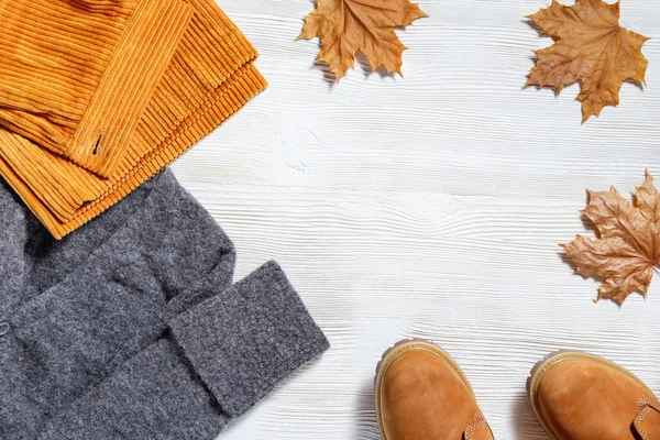 女性秋季服装 时尚橙色皮靴 温暖的针织毛衣和鲜艳的裤子装饰秋天枫叶 平铺着舒适的衣服 把空间复制到白色的木桌上 — 图库照片