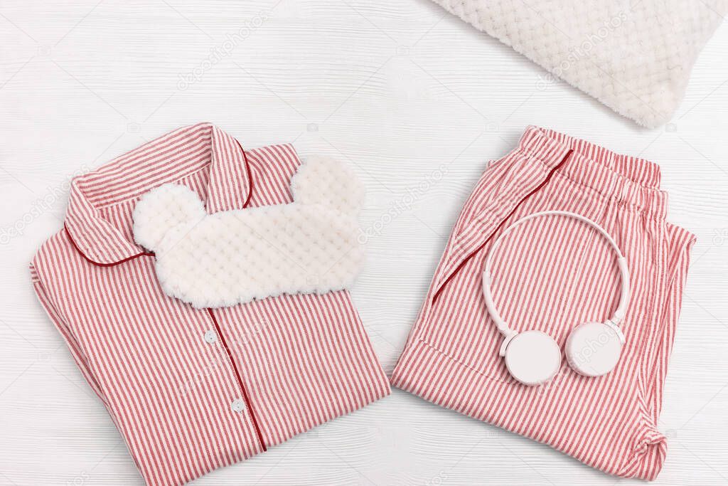 Soft red cotton pajamas with striped pattern. Warm shirt and pants, cushion, sleep mask, headphones. Comfortable wear for home and sleeping. Top view. Flat lay.