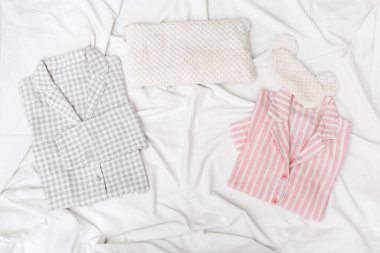 Erkekler ve kadınlar için pembe ve gri pijama ve beyaz pamuklu çarşafta göze göz maskesi. Uyumak için rahat bir ev elbisesi. Üst Manzara. Düz yatıyordu.