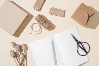 Masada boş sayfalar ve paketleme hediyeleri olan açık defterin üst görünümü, sonbahar konsepti. Evde veya nötr bej tonlu küçük bir ofiste yaratıcı çalışma alanı.