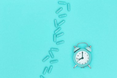 İlaç hapları, zaman kontrolü için kapsül saat naneli kâğıt üzerinde yatıyor. Tıbbi geçmişi var. Üst Manzara. Boşluğu kopyala