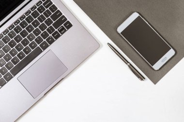 Gri dizüstü bilgisayarı, kalemi ve akıllı telefonu olan beyaz çalışma masasının üst görüntüsü. Okul ya da ofis için çalışma alanı. Uzayı kopyala Düz yatıyordu.