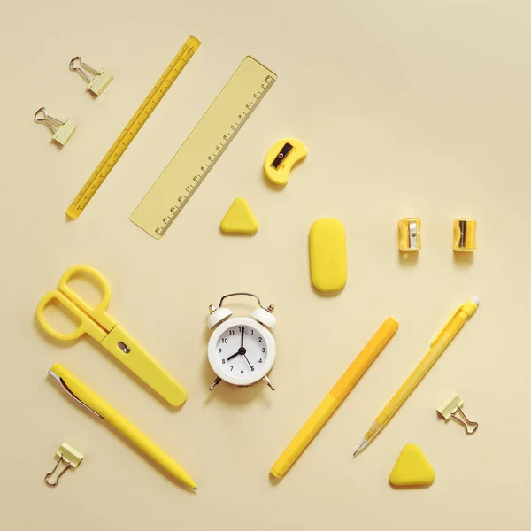 Alarm clock shows 8 oclock in morning, time to go to school concept. Creative Flat lay with clock and stationary school supplies in yellow pastel colored.