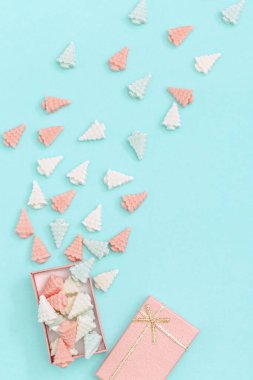 Pastel şeker şekerlemeleri, Noel ağacı şeklinde hediye kutusundan kağıt arka planda en az tarzda dağıtılır. Yeni yıl şablonu pembe tonlarda. Üst görünüm.