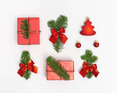 Doğal yeşil ağaç dallarıyla Noel kompozisyonu ve beyaz arka planda kırmızı ambalaj kağıdıyla fiyonk ve hediye kutusu. Yeni yıl tatili dekorasyonu. Düz yatış, üst görünüm.