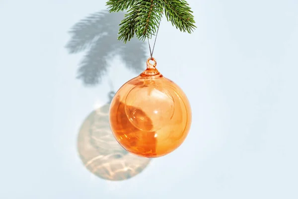 新年やメリークリスマスの背景 青い色の壁に松の枝にぶら下がっているオレンジ色の透明な丸いボール コピースペース付きの最小限のスタイルの背景 — ストック写真
