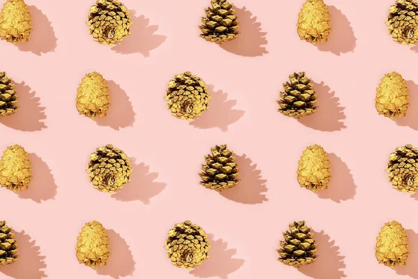 Natural pine cones golden colored as New Year pattern. Bright Christmas holidays decor on tender pink paper.