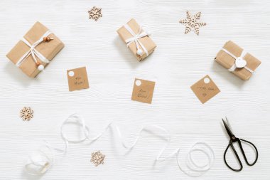 Noel ve yeni yıl için el yapımı Noel hediye kutusunu etiketlerle hazırlıyorum. Firavun dalları, kurdele, makas beyaz ahşap masada. Düz yatıyordu. Üst görünüm.