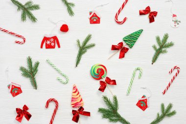 Noel tatlıları çeşitli üst manzara, yeşil köknar dalları, beyaz arka planda tahta oyuncaklar, düz bir zemin. Parlak yeni yıl şekeri ve lolipopları.