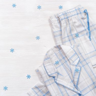 Üzerinde mavi çekler olan katlanmış beyaz pijamalar ya da beyaz tahta arka planda fotokopi alanı olan çizgiler. Gece giysisi kış tatili için süslenmiş kar taneleri. Düz yatıyordu.