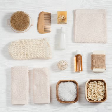 Doğal malzemeden banyo aksesuarları, banyo için sıfır atık seti, pamuk havlular, jöle ve şampuanlı küçük şişeler, sabun, deniz tuzu, beyaz ahşap masadaki bez..
