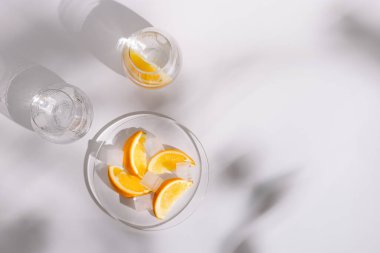 Güzel cam bardaklarda doğal su ve buz içmek ve beyaz arka planda bir dilim taze portakal yemek. Sert gölgelerle bezenmiş yaz ayları. Üst görünüm.