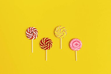 Sarı kağıtta çizgili şeker lolipopları var. Yaratıcı konsept hala doğum günü, parti, tatiller için hayat tatlısı. Üst görünüm ve düz uzanma.