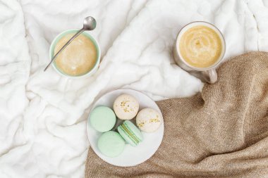 Sütlü kahve ve lezzetli badem kurabiyeleri ışık masasında. Birkaç kişi için sıcak bir sabah içkisi. Kopyalama alanı olan üst görünüm.