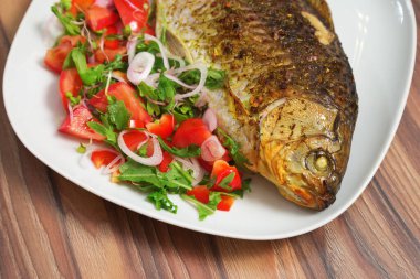 Balık yemeği. Beyaz tabakta kavrulmuş sazan balığı ve taze sebze. Yakın planda kızartılmış haç hazır. Sıcak yemek. Ana yemek..