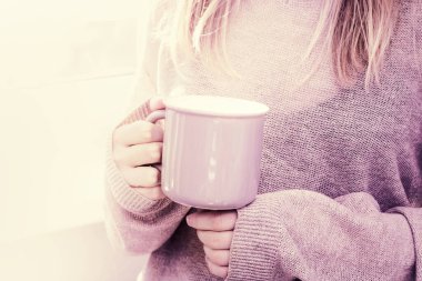 Kahve fincanı, örgü süveter giymiş kadınların elinde. Elinde sıcak kahve tutan ve gün ışığıyla pencerenin önünde duran bir kadın. Sabah kahvesi. Yaşam tarzı. Kopyalama alanı olan sosyal medya içeriği.