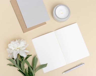 Masanın yukarıdan görünüşü açık defter ve aromatik mum ile süslenmiş doğal beyaz şakayık çiçeği. Yaz zamanı çalışma veya eğitim konsepti, blog sosyal medya için şablon.