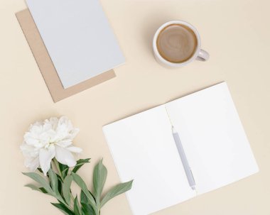 Masanın yukarıdan görünüşü, açık defter, fincan kahve, doğal beyaz şakayık çiçeği. Yaz zamanı çalışma veya eğitim konsepti, blog sosyal medya için şablon.