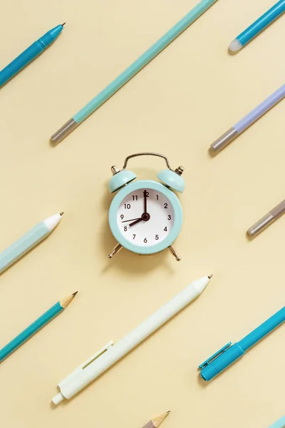 目覚まし時計午前8時 学校の概念に移動する時間を示しています ベージュ地に青いペンと鉛筆の時計と幾何学模様の創造的なフラットレイ — ストック写真