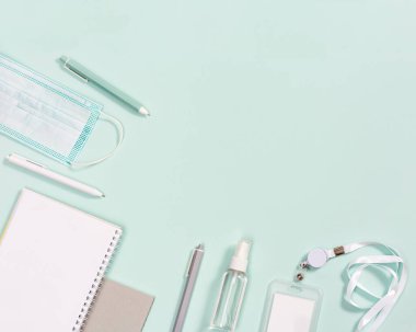 Ofis malzemeleri, defterler, kalemler, enfeksiyonlardan korunmak için maske ve temiz arka planda el dezenfektanı. Yukarıdan görüntüle.