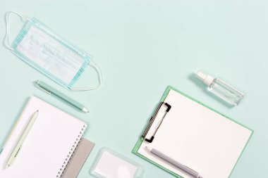 Okul aksesuarları, yeni normal kavram, tıbbi maske ve naneli kağıt arka planda el dezenfektanı. Kapat, üst görünüm.