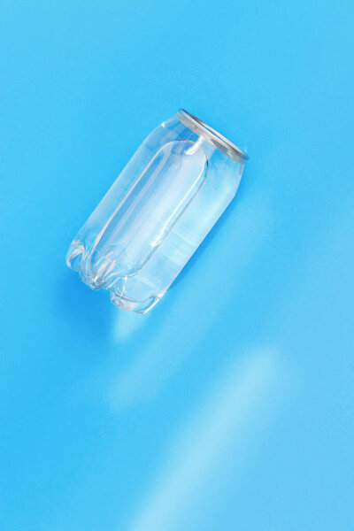 Transparent can of water with sunlight on blue background. Monochrome image. Creative idea, new package of clear water in plastic bottle as can. Top view.