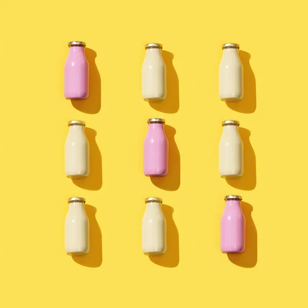 Creative pattern with small glass bottles for juice or yogurt. Packaging template mock up on yellow colored background with hard light.