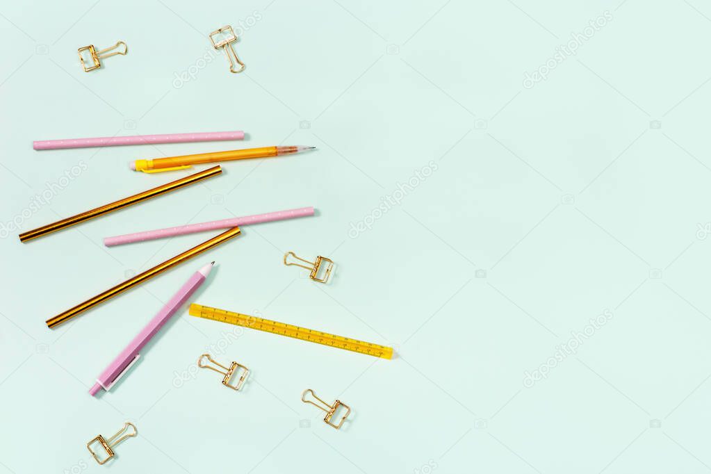 Flat lay with stationery for school or office. Pink and golden colored pencils, pens and metal paperclips. School equipment. Top view with copy space.