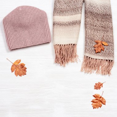 Sonbahar konforlu kıyafetler ve dekoratif sarı kırmızı yapraklar. Beyaz ahşap arka plandaki kadınlar için eşarp ve şapka. Üst görünüm.