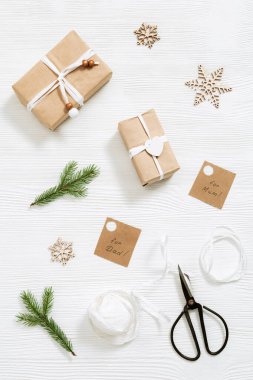 Noel ve yeni yıl için el yapımı Noel hediye kutusunu etiketlerle hazırlıyorum. Firavun dalları, kurdele, makas beyaz ahşap masada. Düz yatıyordu. Üst görünüm.